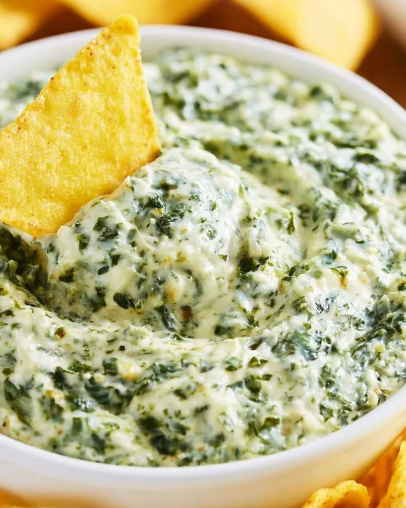 Dip de espinacas cremoso servido en un bol con galletas alrededor.